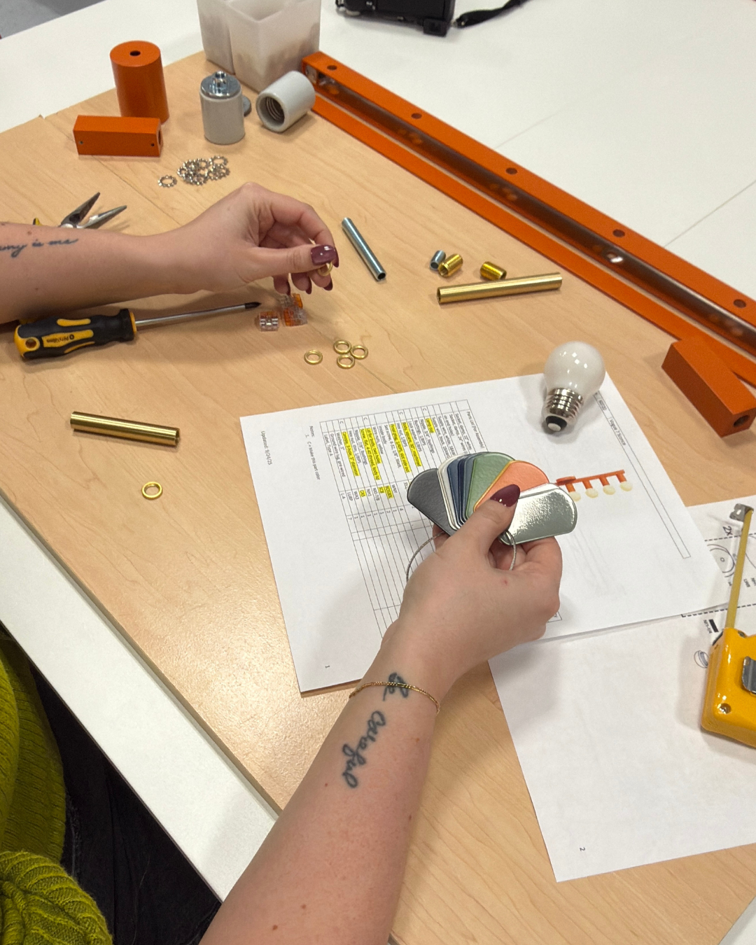 Hand over a table with blueprints, color samples, lightbulbs, etc