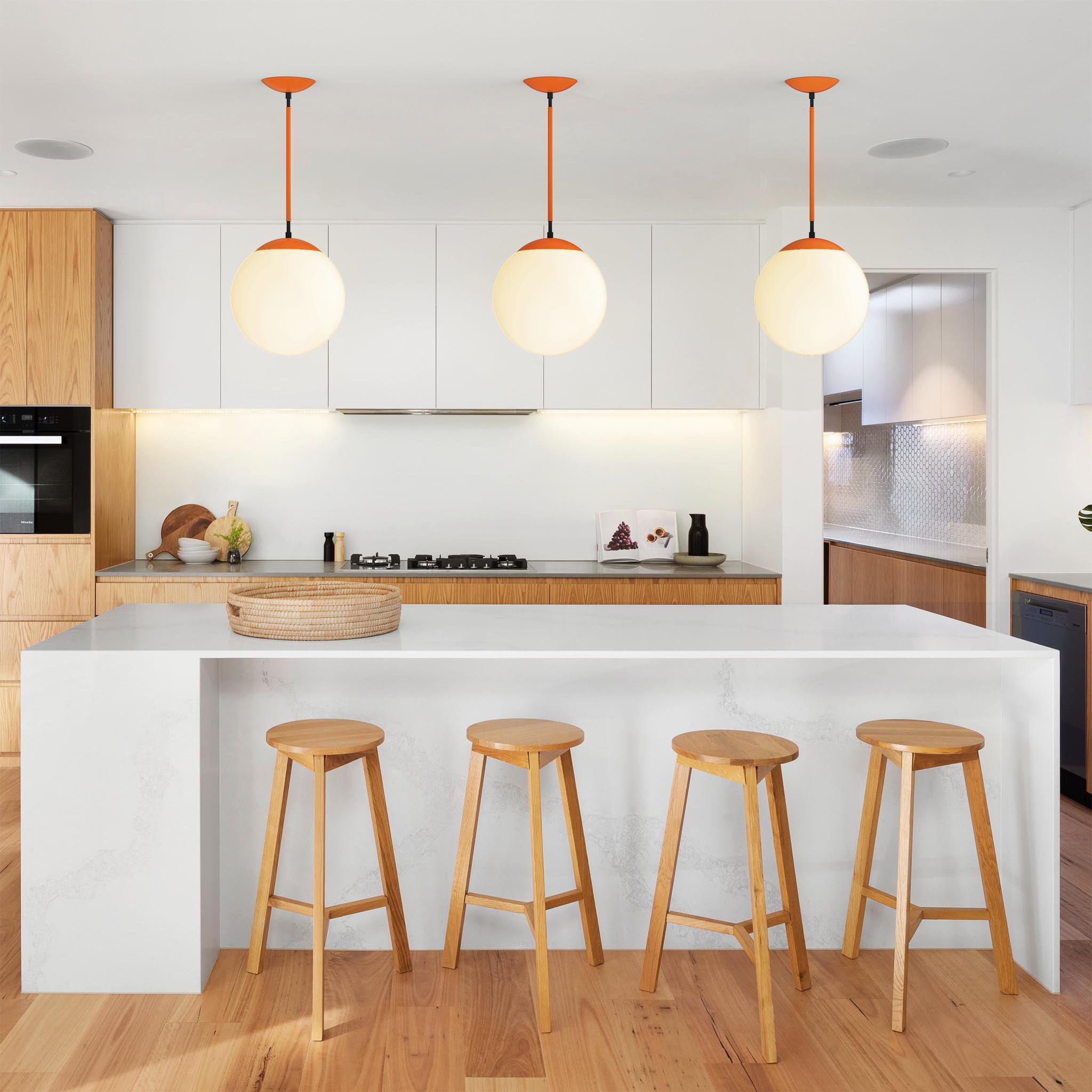 Three Cap Pendants (orange and black) hanging over a kitchen island. 