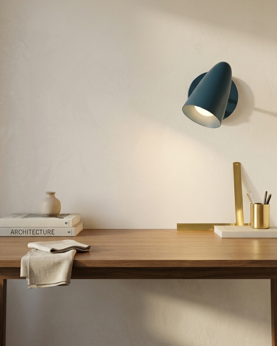 Modern desk setup with a lamp, books, and a vase against a plain wall.